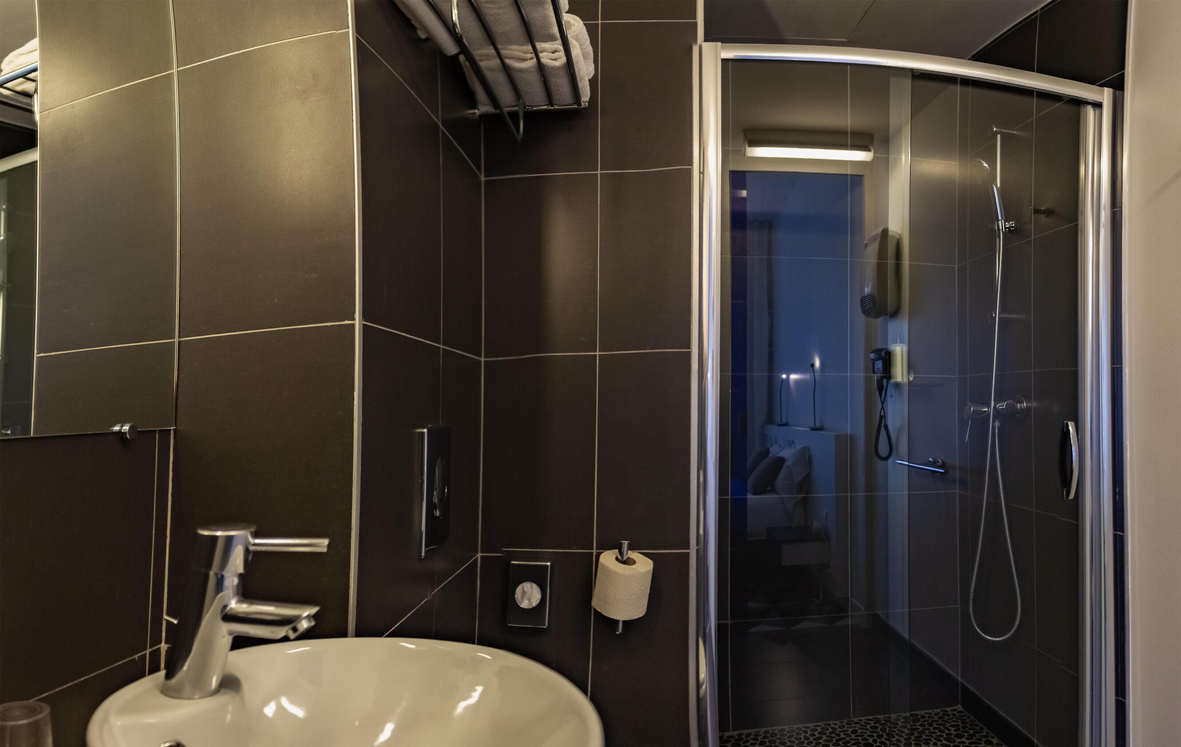 A modern bathroom with a curved shower enclosure, a white sink, and dark tiled walls.