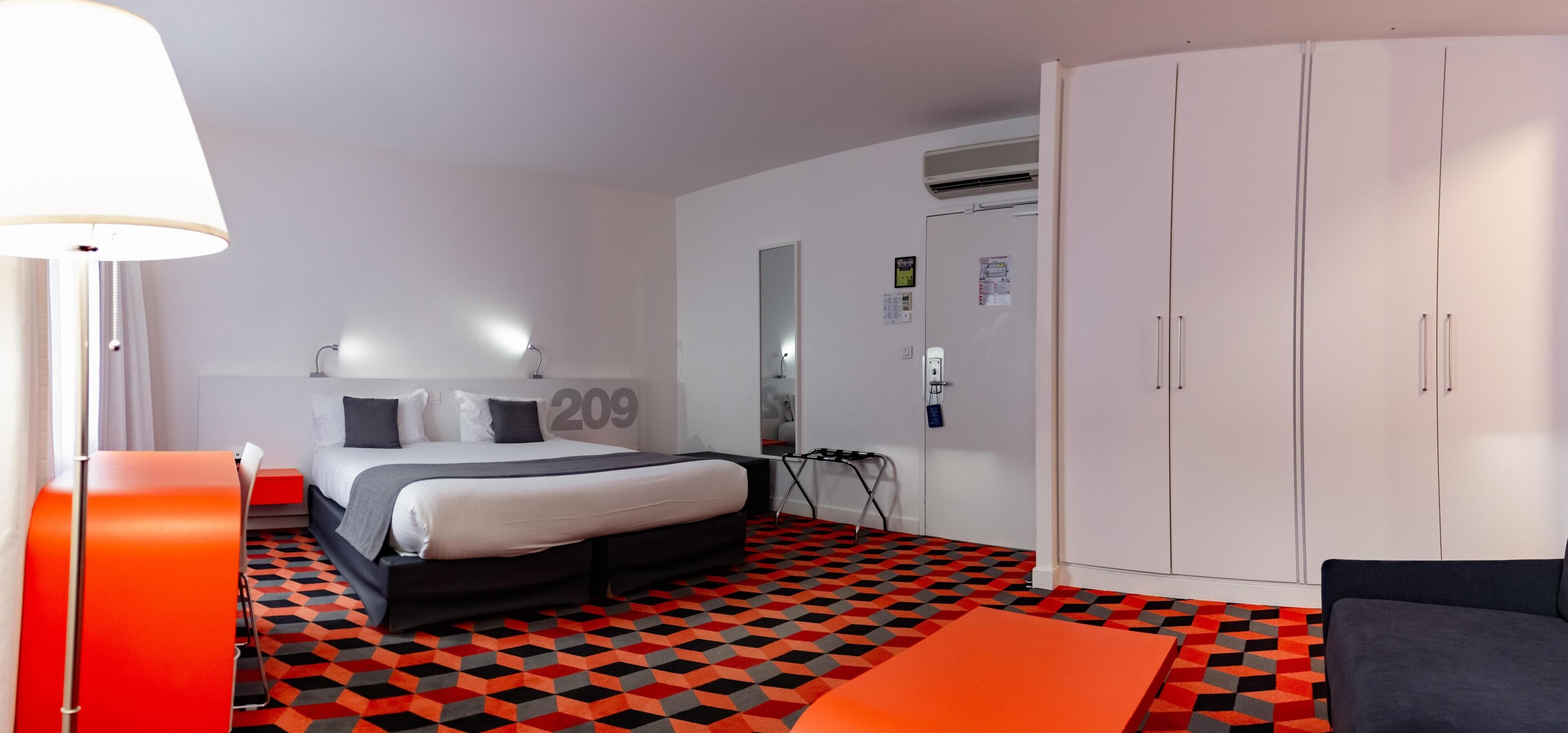 Una habitación de hotel con cama, escritorio, silla, armario y suelo estampado.