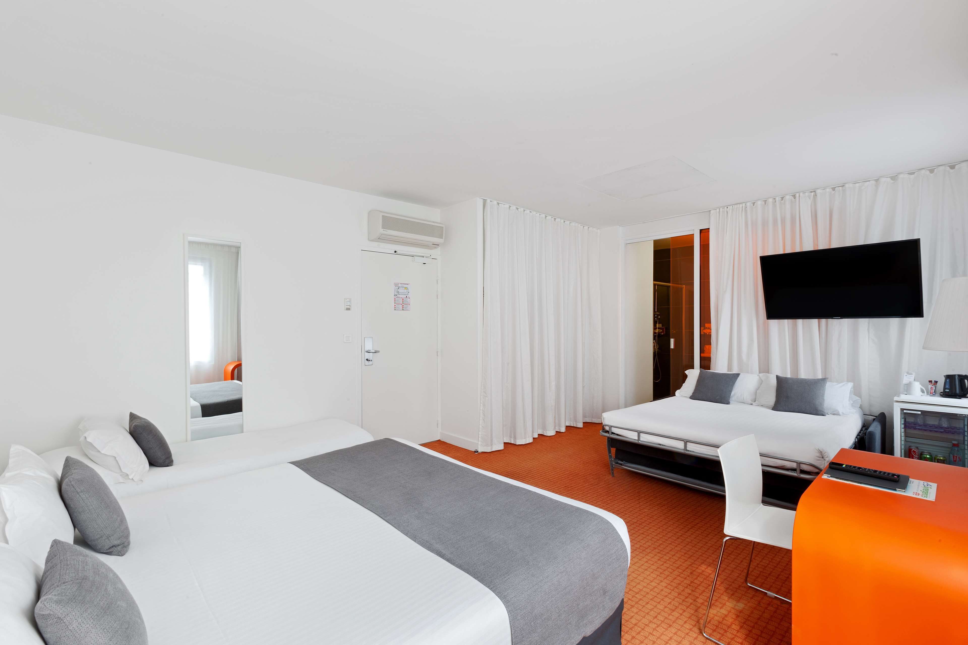 A hotel room with a bed, a desk with a chair, a TV, and a window with curtains.
