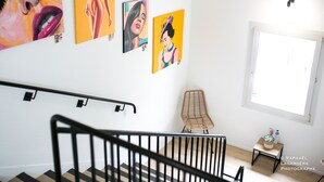 Eine Treppe mit Handlauf, ein gewebter Stuhl und Kunstwerke an der Wand.
