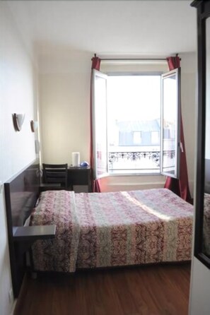 A bedroom with a bed, a nightstand, a window with curtains, and a view of a balcony. - Hipotel Paris Printania Maraîchers (Paris)