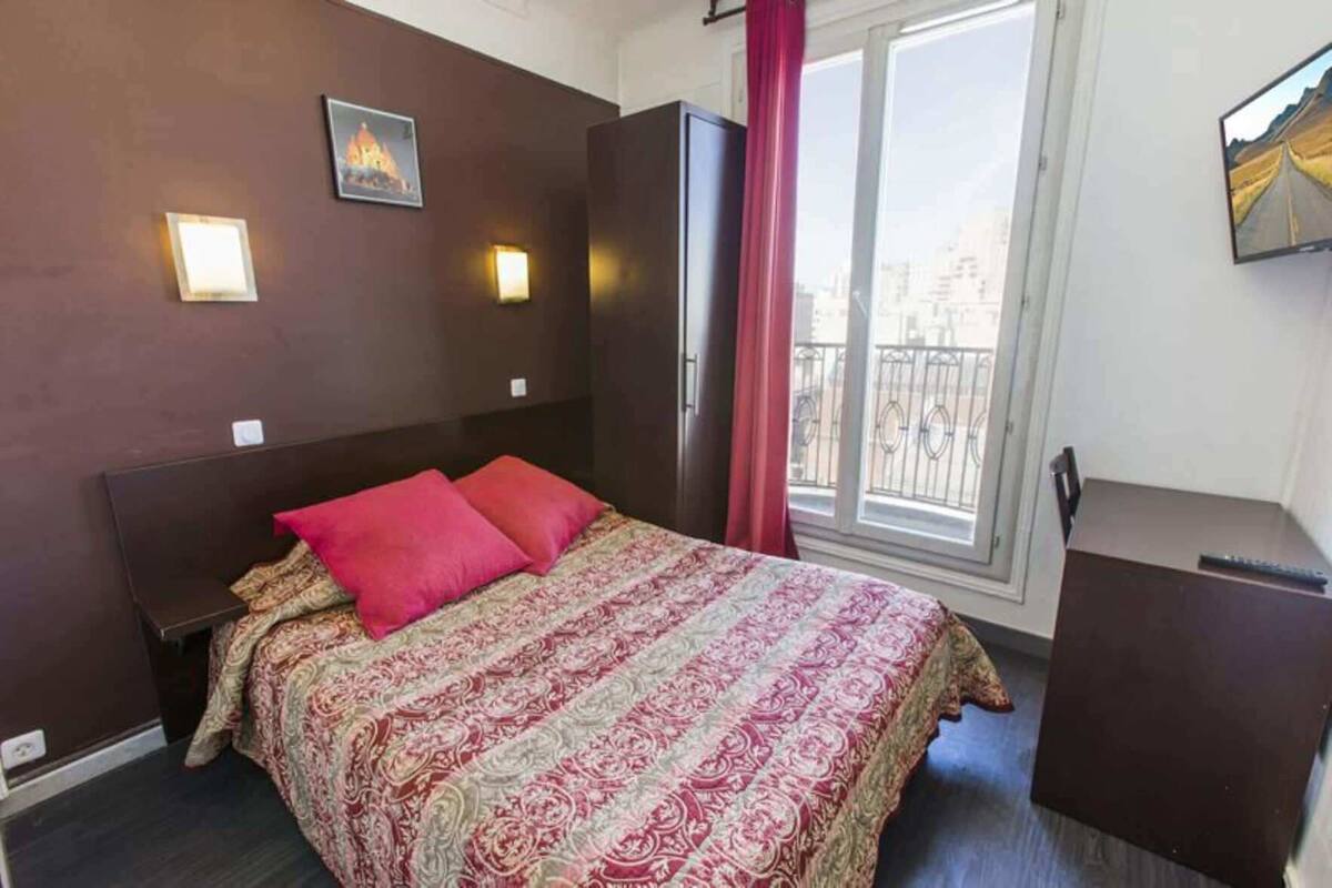 Una habitación de hotel con cama, mesita de noche, cómoda, ventana con vistas y luces en la pared.
