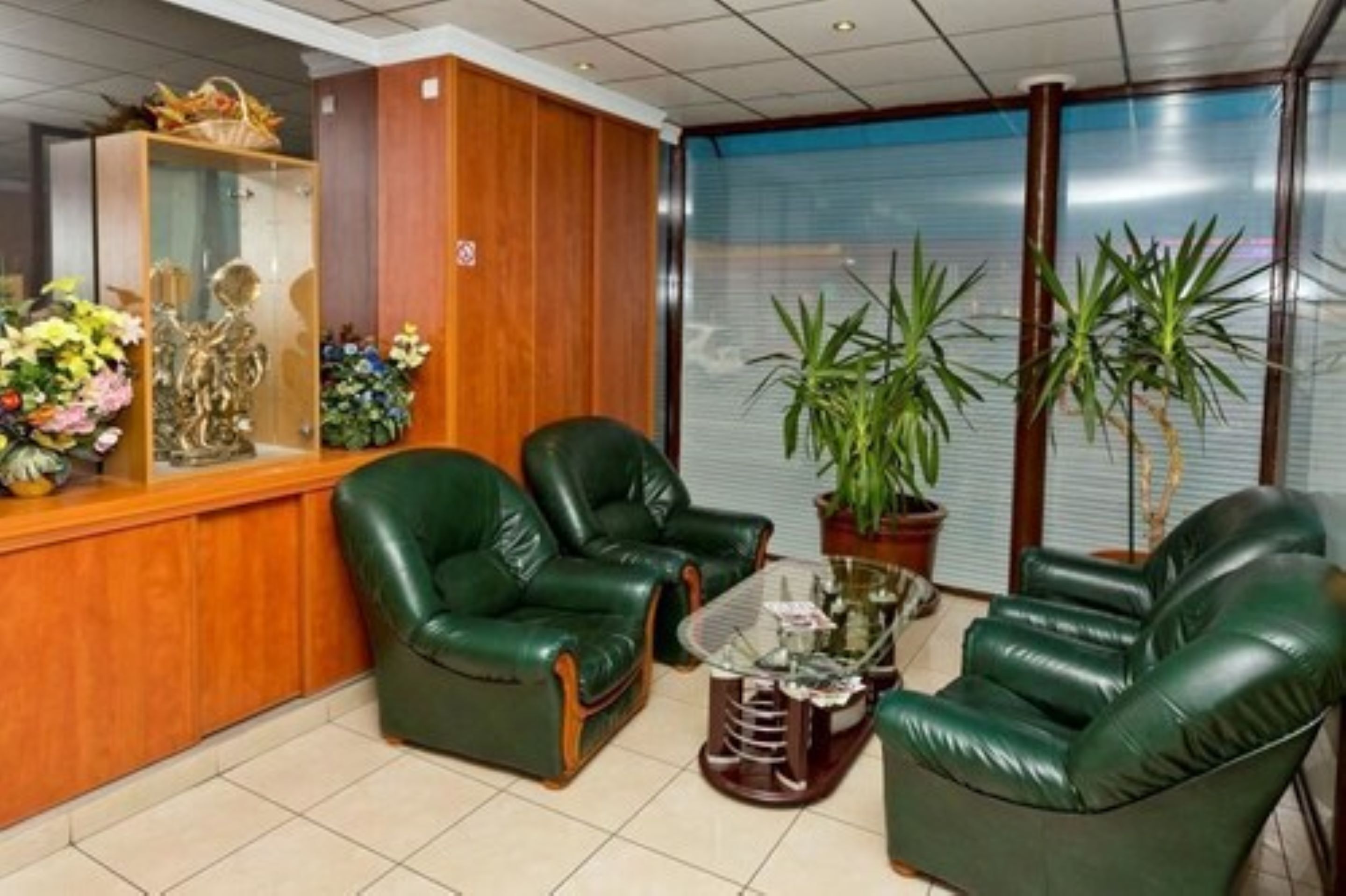 A reception area with green leather chairs, a glass coffee table, and a wooden reception desk with a glass display case.