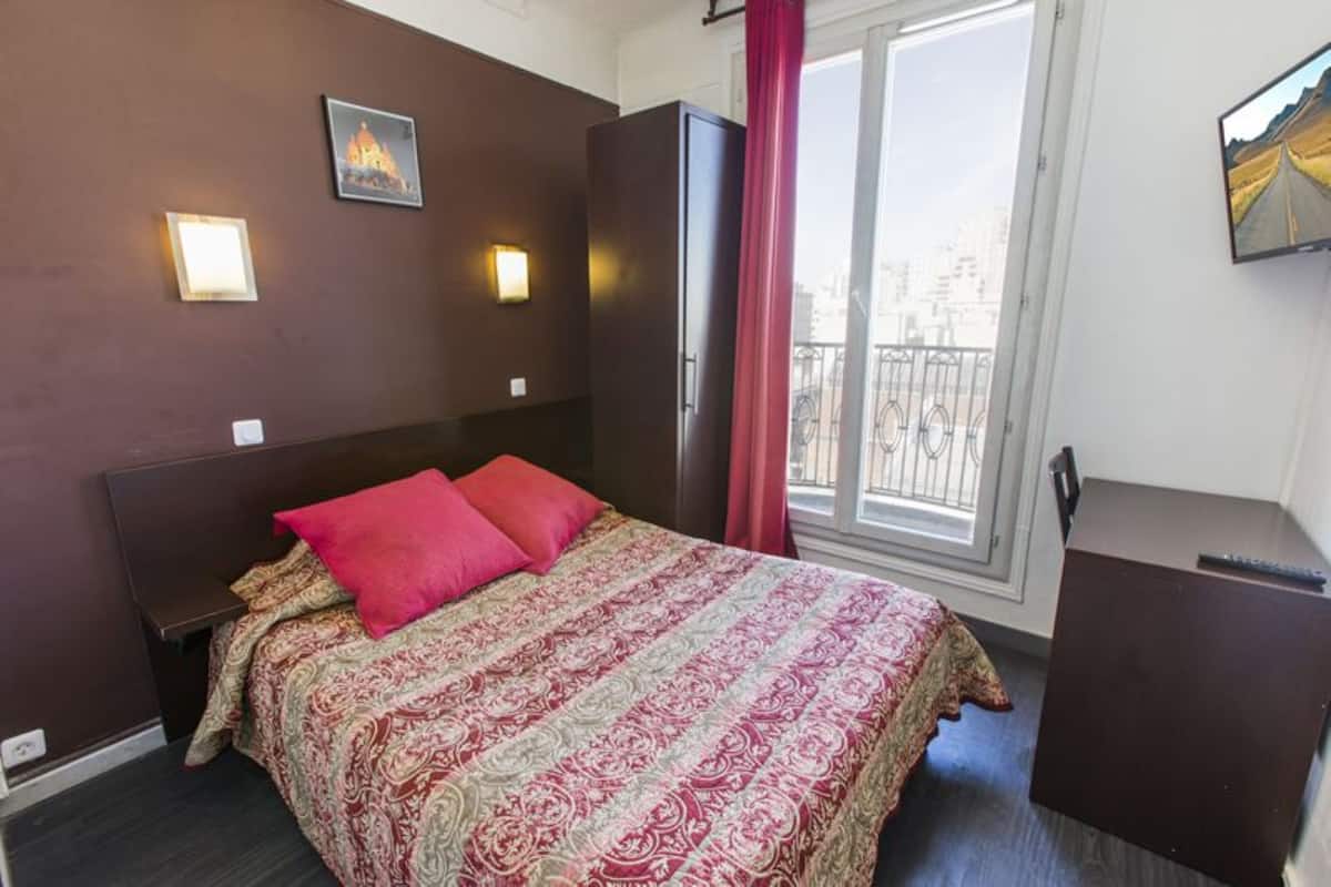 Habitación de hotel con una cama grande, un armario, un escritorio y una ventana con vista a la ciudad.