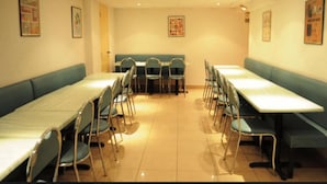 A dining area with long tables and chairs, a central booth, and framed pictures on the walls. - Hipotel Paris Printania Maraîchers (Paris)