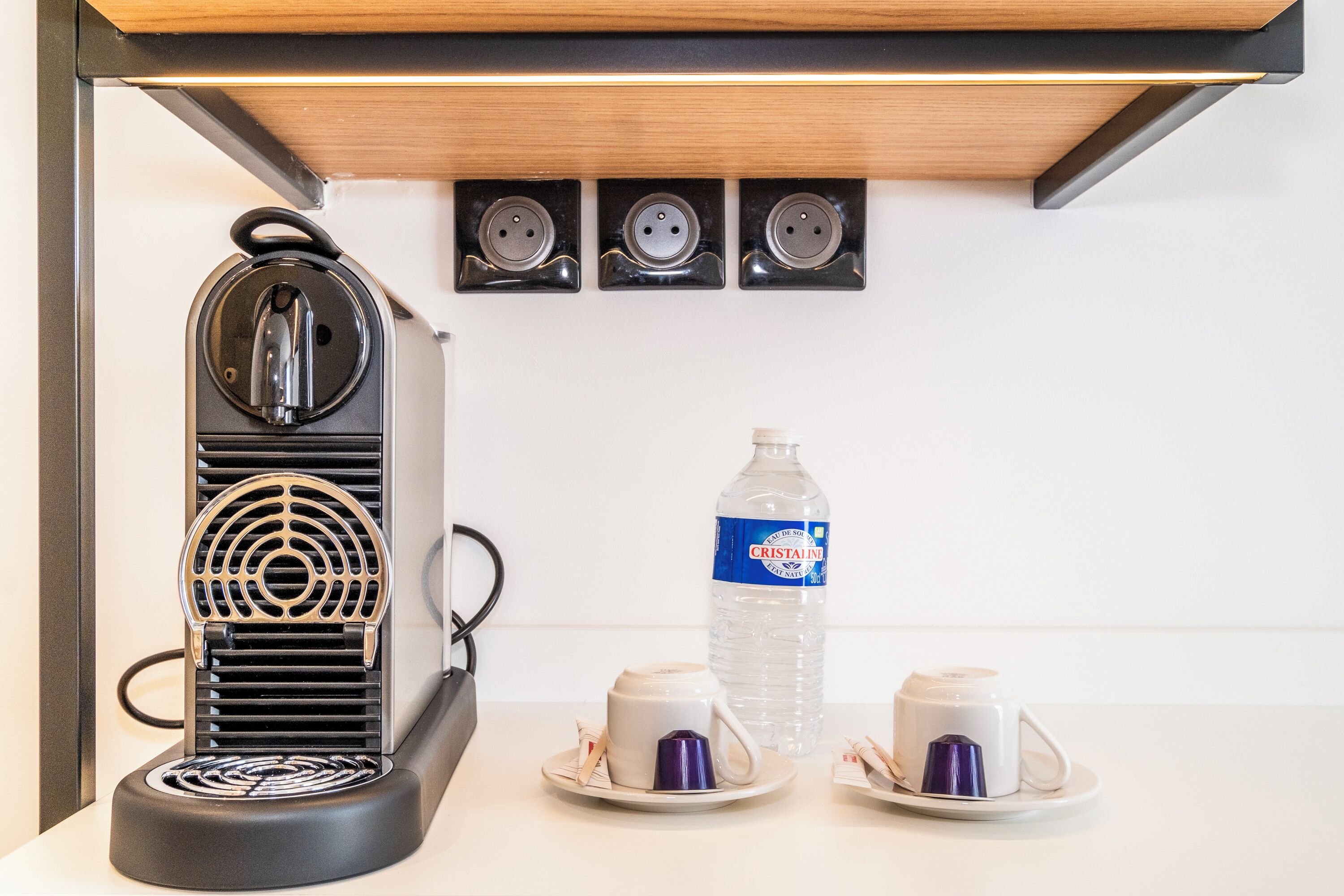 A coffee machine with a water bottle and two cups on a white countertop.
