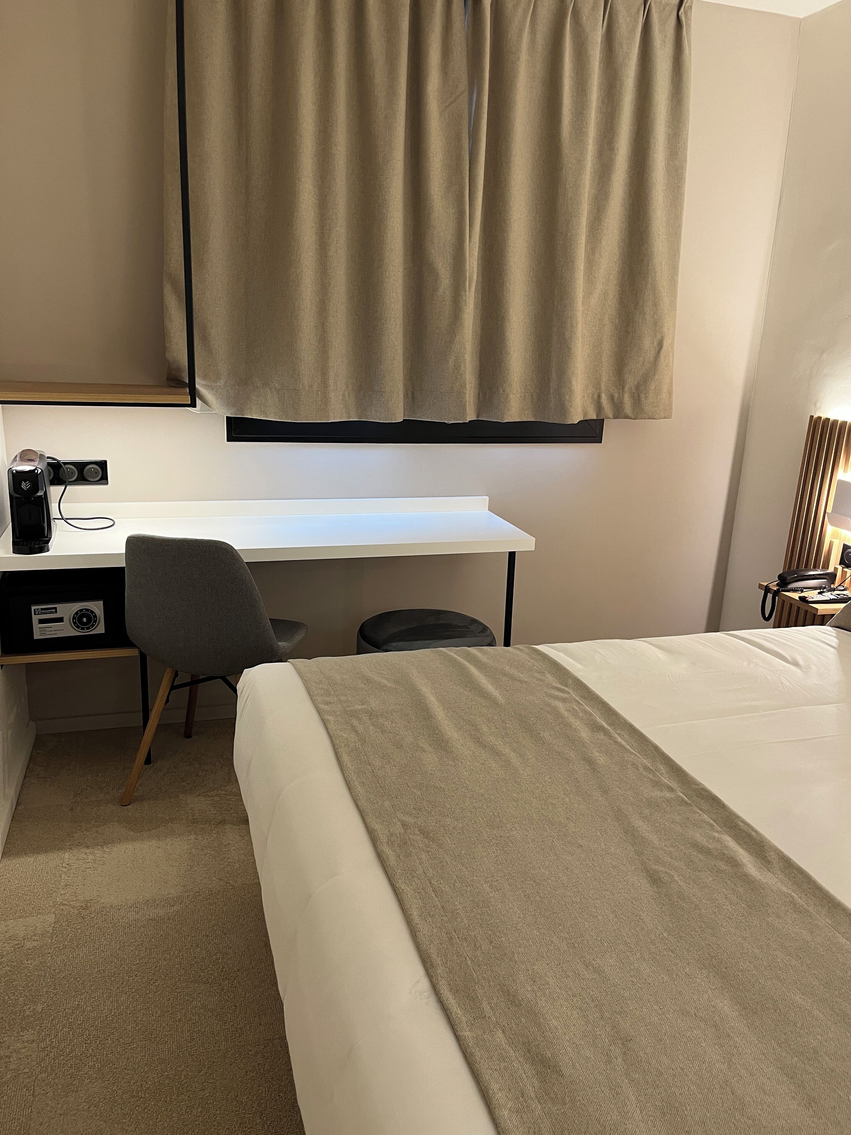 Una habitación de hotel con una cama, un escritorio con una silla, una cafetera y una lámpara.