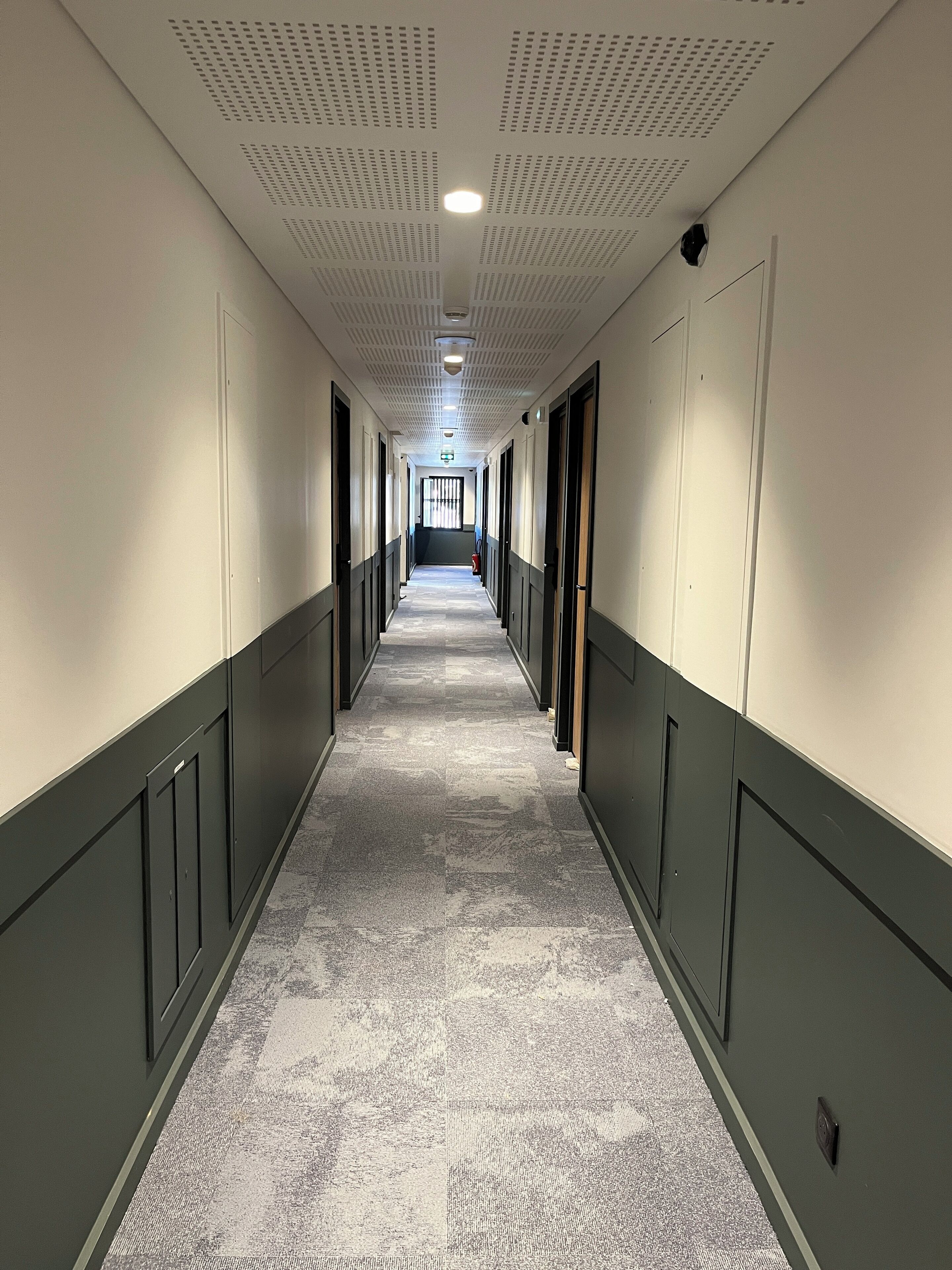 A long, narrow hallway with a patterned carpet, white walls, and doors on both sides.