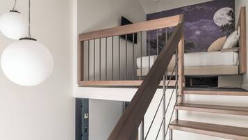 Una escalera moderna con peldaños de madera y barandillas metálicas, que conduce a un dormitorio en loft con un mural del cielo nocturno.