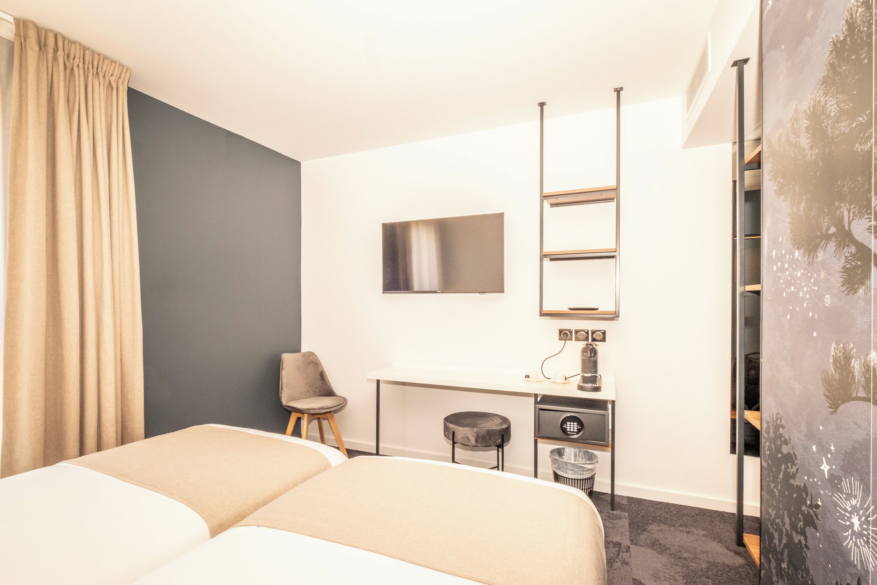 Habitación de hotel con cama, escritorio, silla, taburete pequeño, cesto de basura y espejo.