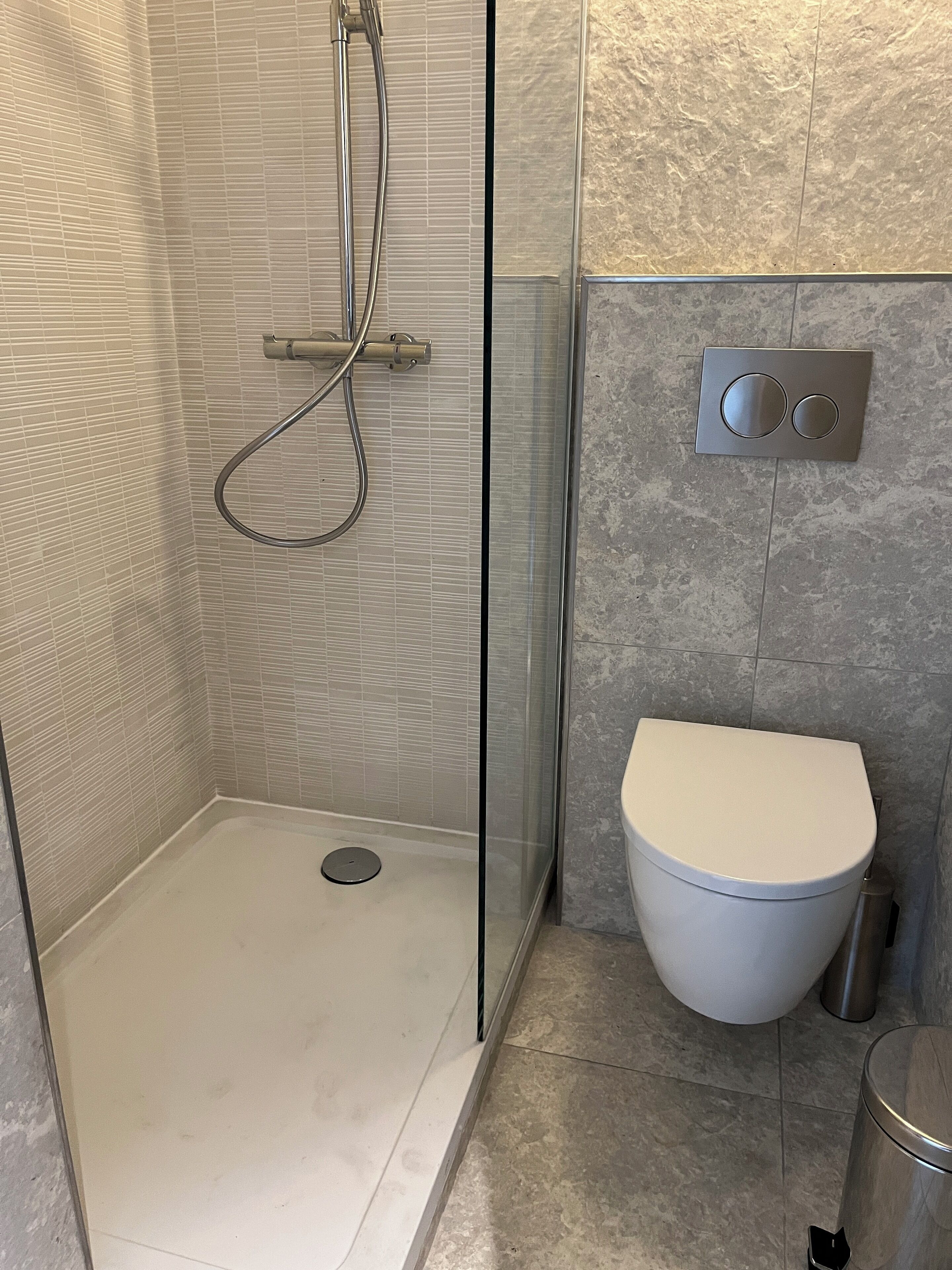 Ein modernes Badezimmer mit einer gläsernen Duschkabine, einer weißen Toilette und einer wandmontierten Bedienkonsole.