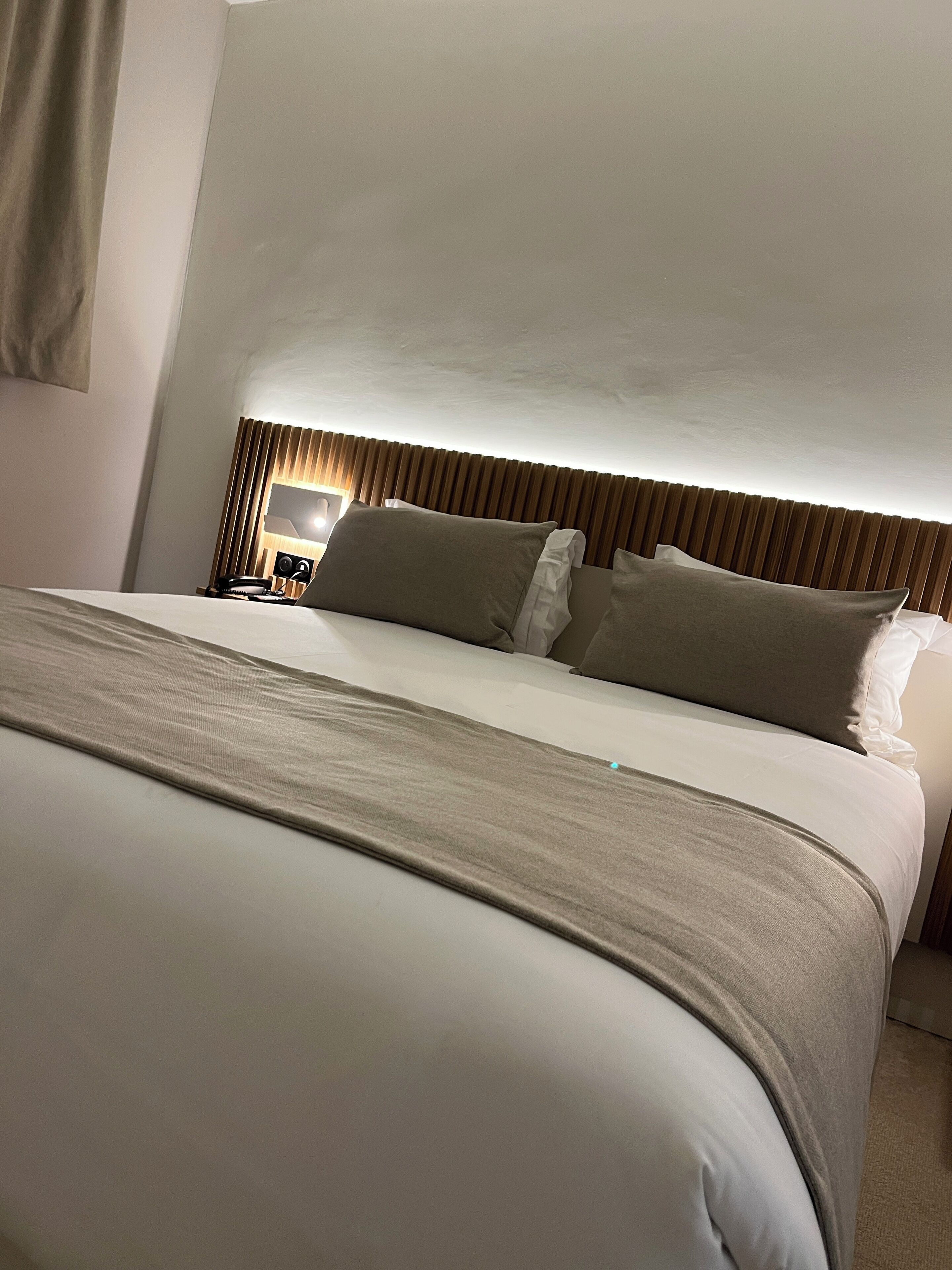 A neatly made bed with a headboard, a bedside table with a lamp, and a wall-mounted artwork.