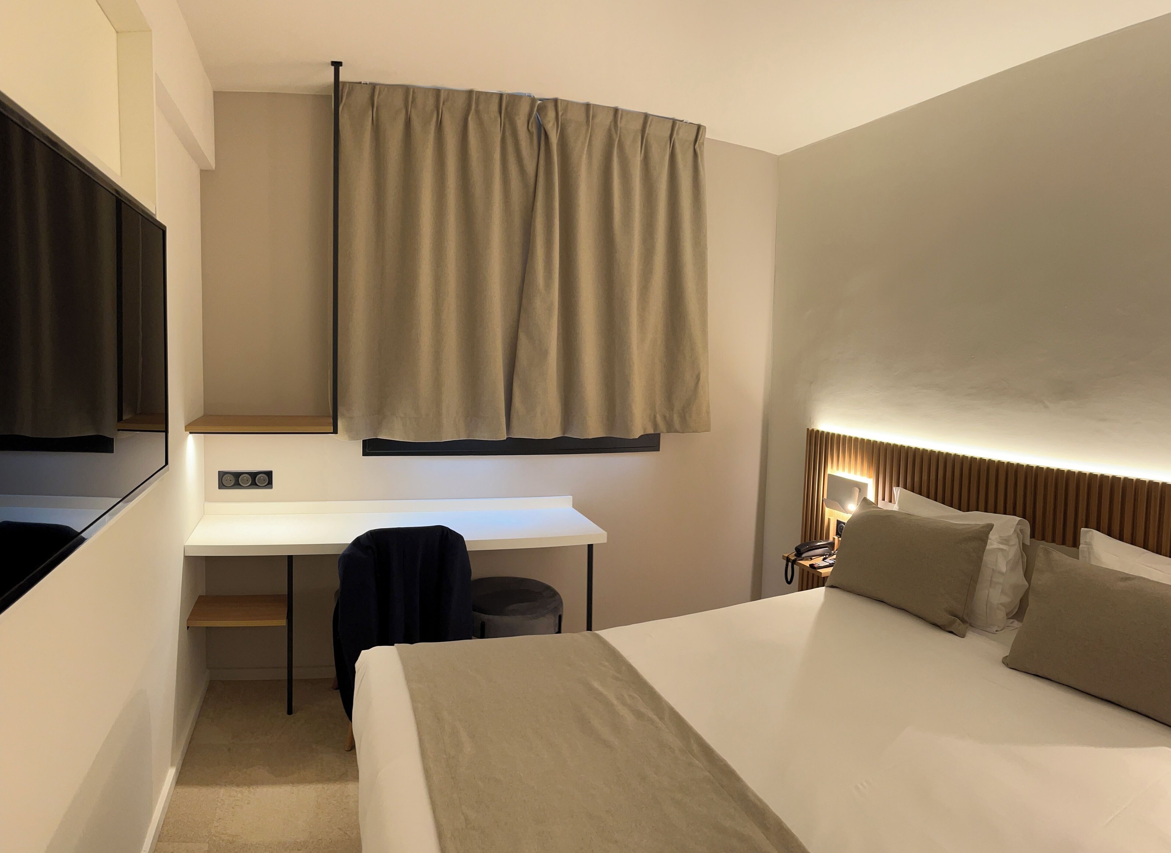 A hotel room with a bed, a desk, a chair, a lamp, and a mirror.