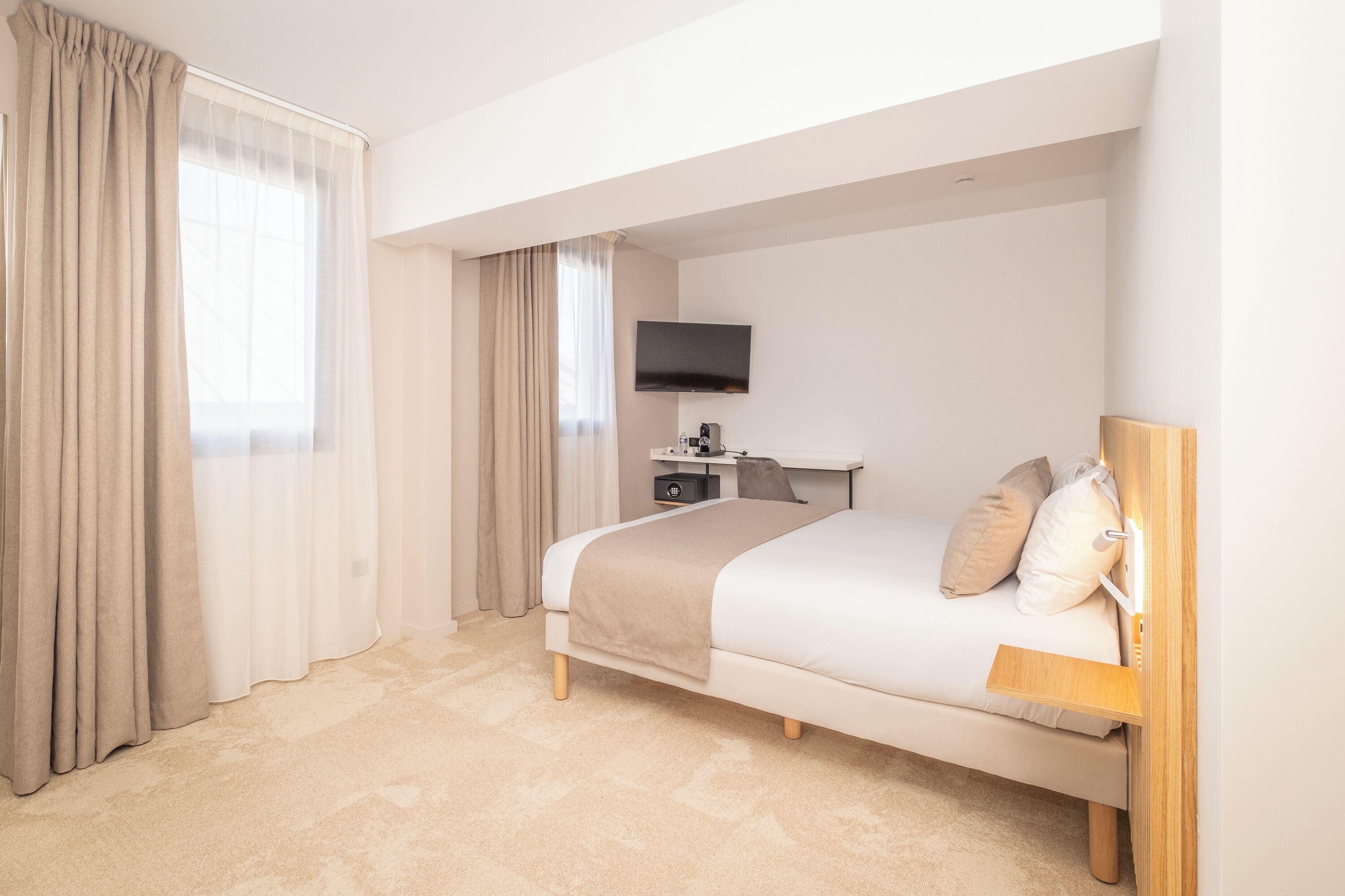 A bedroom with a bed, a desk, a television, and a window with curtains.