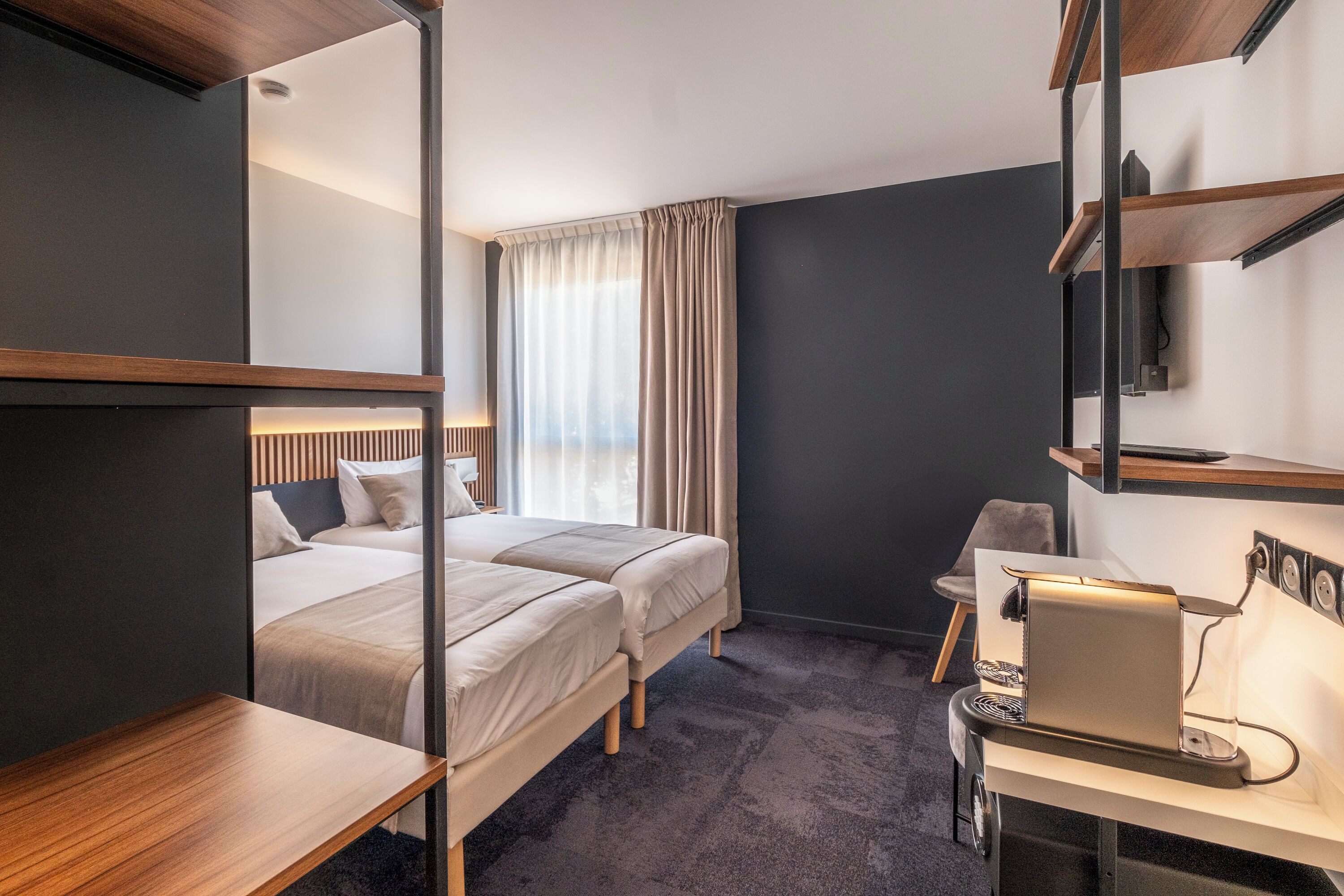 Una habitación de hotel moderna con dos camas, un escritorio, una silla y un televisor fijado a la pared.