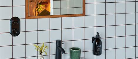 A bathroom with a white sink, a mirror, a green vase, and a black bottle on the wall.