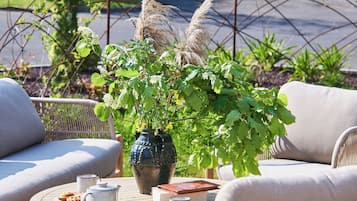 A deck with wicker furniture, a table with a teapot, a book, and a vase with plants.