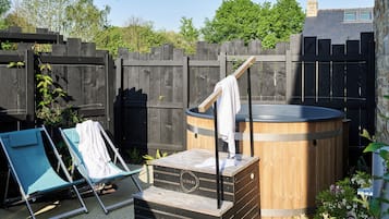 A hot tub with a wooden base and a metal frame, surrounded by a wooden fence and greenery.