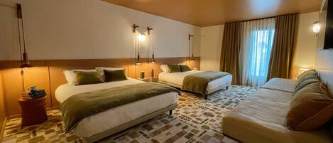 A hotel room with two beds, a sofa, patterned carpet, and wall-mounted lamps.