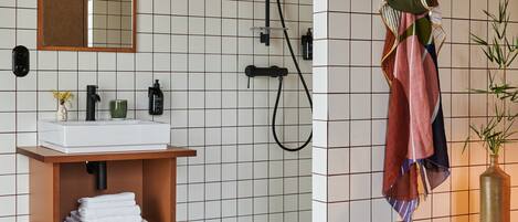Une salle de bain moderne avec un mur recouvert de carreaux blancs, un meuble-lavabo en bois, un miroir, une douche et un porte-serviettes mural.