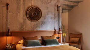 Un dormitorio con una cama grande, cabecera, un adorno circular en la pared, una mesita de noche con lámpara, y una silla.