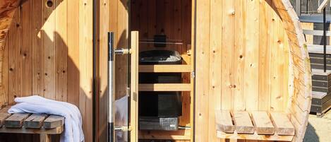 Uma sauna de madeira com porta de vidro, um banco e uma toalha sobre uma mesa.