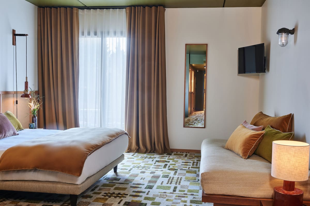 Habitació d'hotel amb llit, sofà, mirall i làmpada.