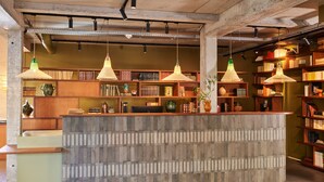 Zona de recepción con mostrador central, lámparas colgantes y estanterías llenas de libros y objetos decorativos.