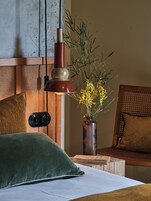 A bedroom with a bed, a bedside table, a lamp, a vase with flowers, and a wall-mounted camera.