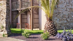 Un edificio de piedra de dos plantas con un balcón, una palmera y un jardín lleno de flores.