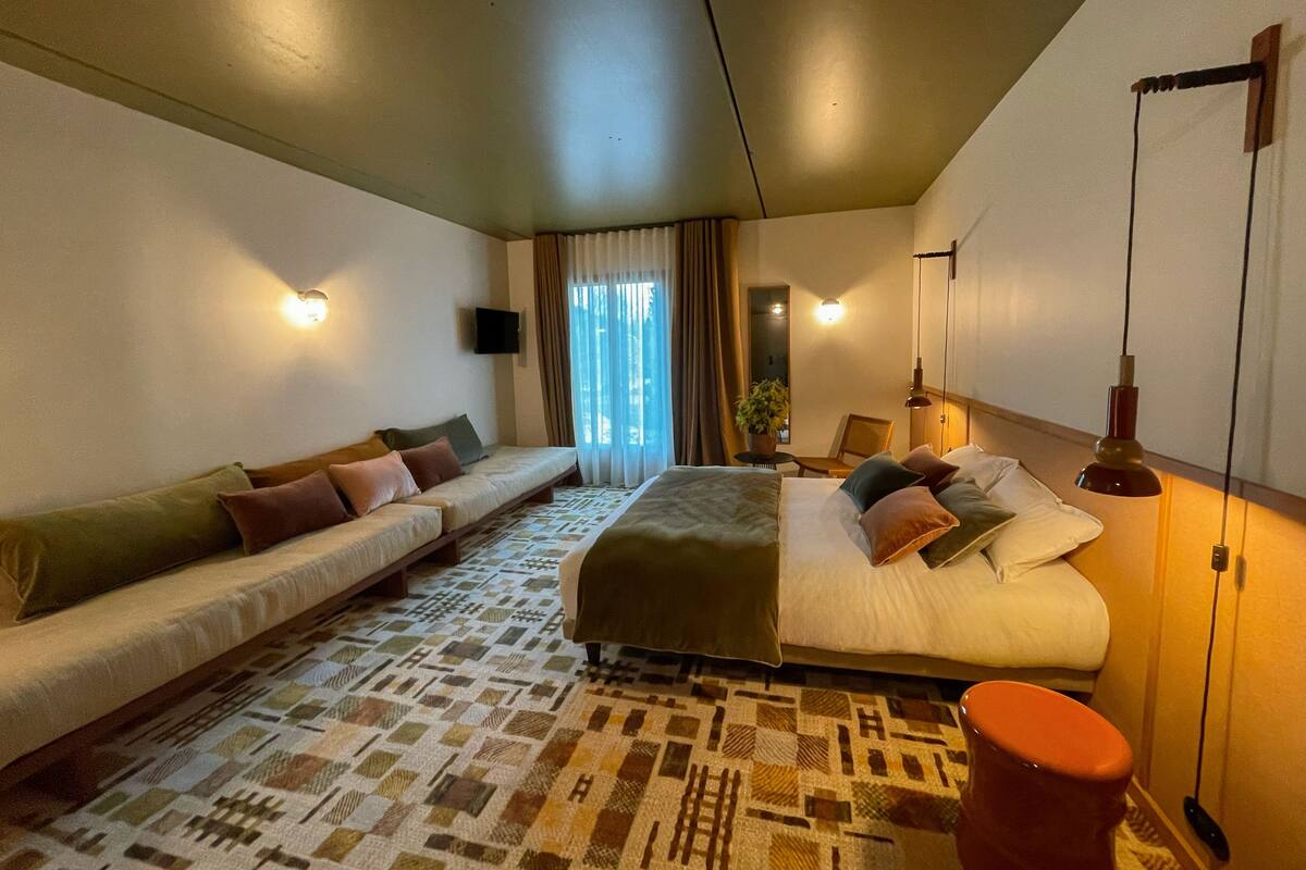 Habitació d'hotel amb llit, sofà, taula petita amb una planta i cadira.