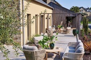 A wooden deck with wicker furniture, a potted plant, and a view of a stone building. - Hôtel Oré (Saint-Malo)