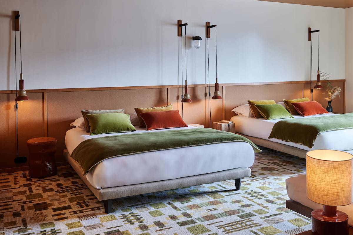 Habitació d'hotel amb dos llits, una catifes amb disseny i il·luminació penjada a la paret.