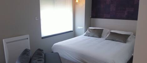 Un dormitorio con una cama, una ventana con persianas, una lámpara fijada a la pared y un radiador.