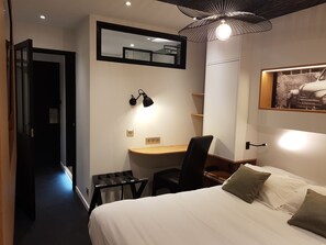 Une chambre d’hôtel comprenant un lit, un bureau, une chaise, une petite table, un miroir et un luminaire au plafond.