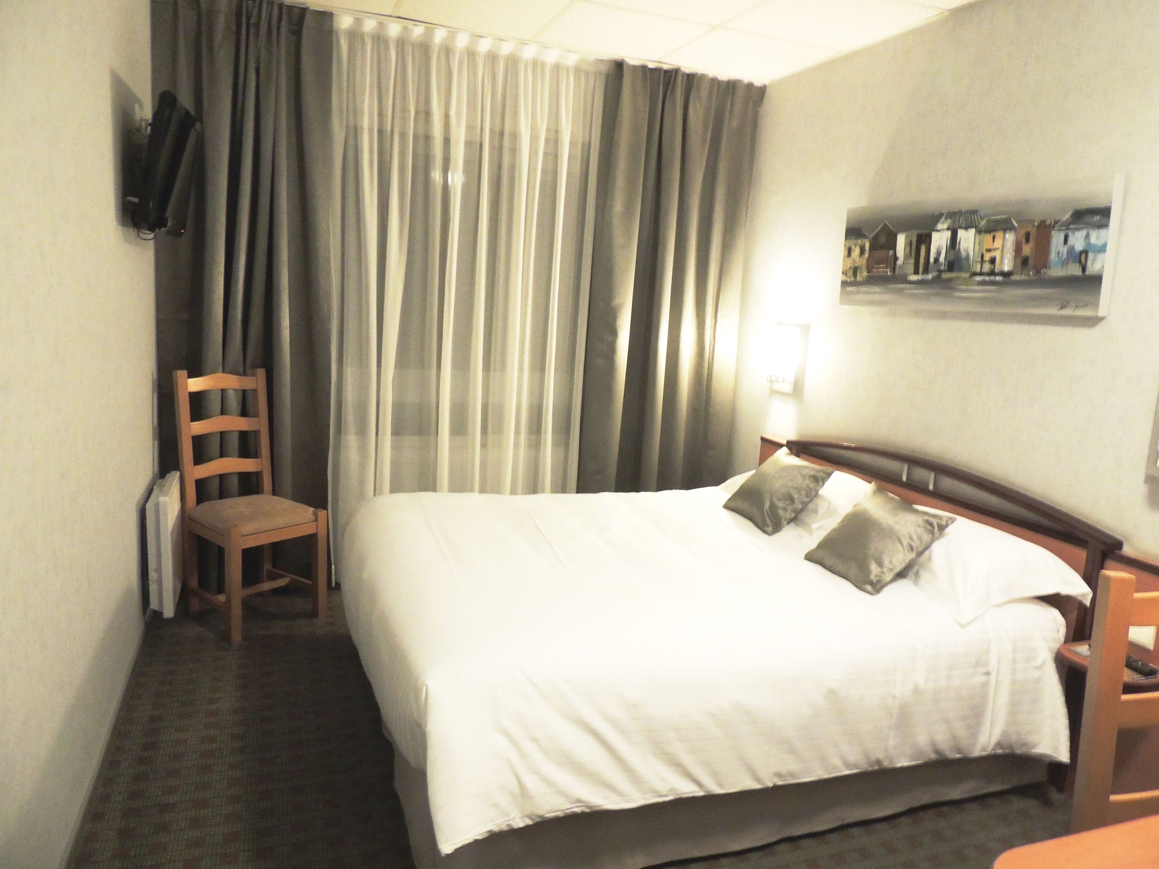 A hotel room with a bed, a chair, a TV mounted on the wall, and a painting on the wall.