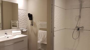 Een moderne badkamer met een glazen douchecabine, een witte handdoekhouder, een haardroger en een spiegel met een structuurwanddesign.