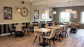 A spacious dining area with multiple tables and chairs, featuring a modern design with pendant lighting and artwork on the walls.