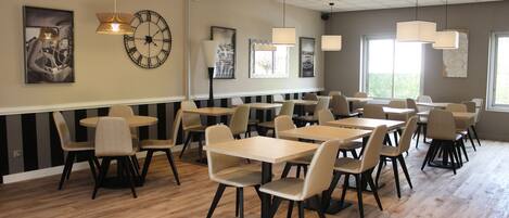 A spacious dining area with multiple tables and chairs, featuring a modern design with pendant lighting and artwork on the walls.