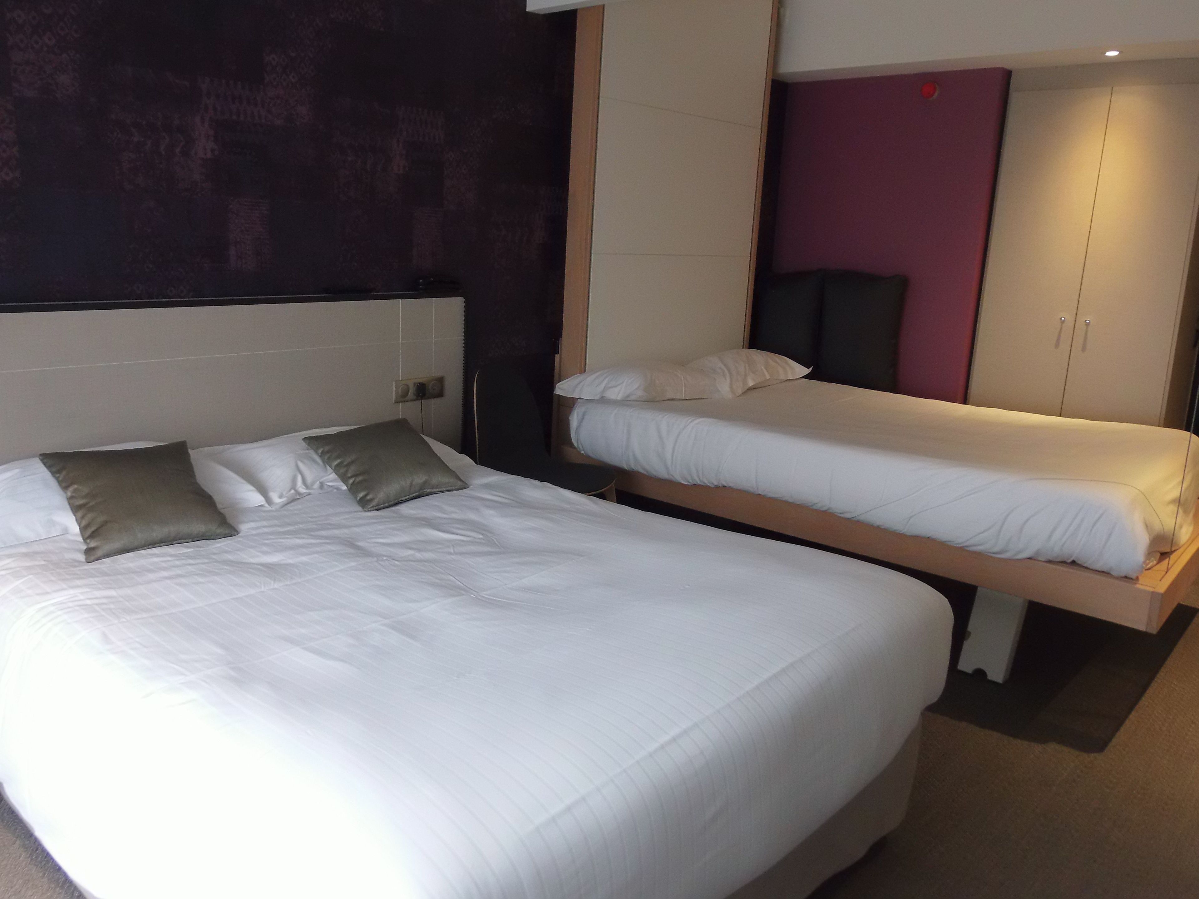 A hotel room with two single beds, a large bed, and a wardrobe.