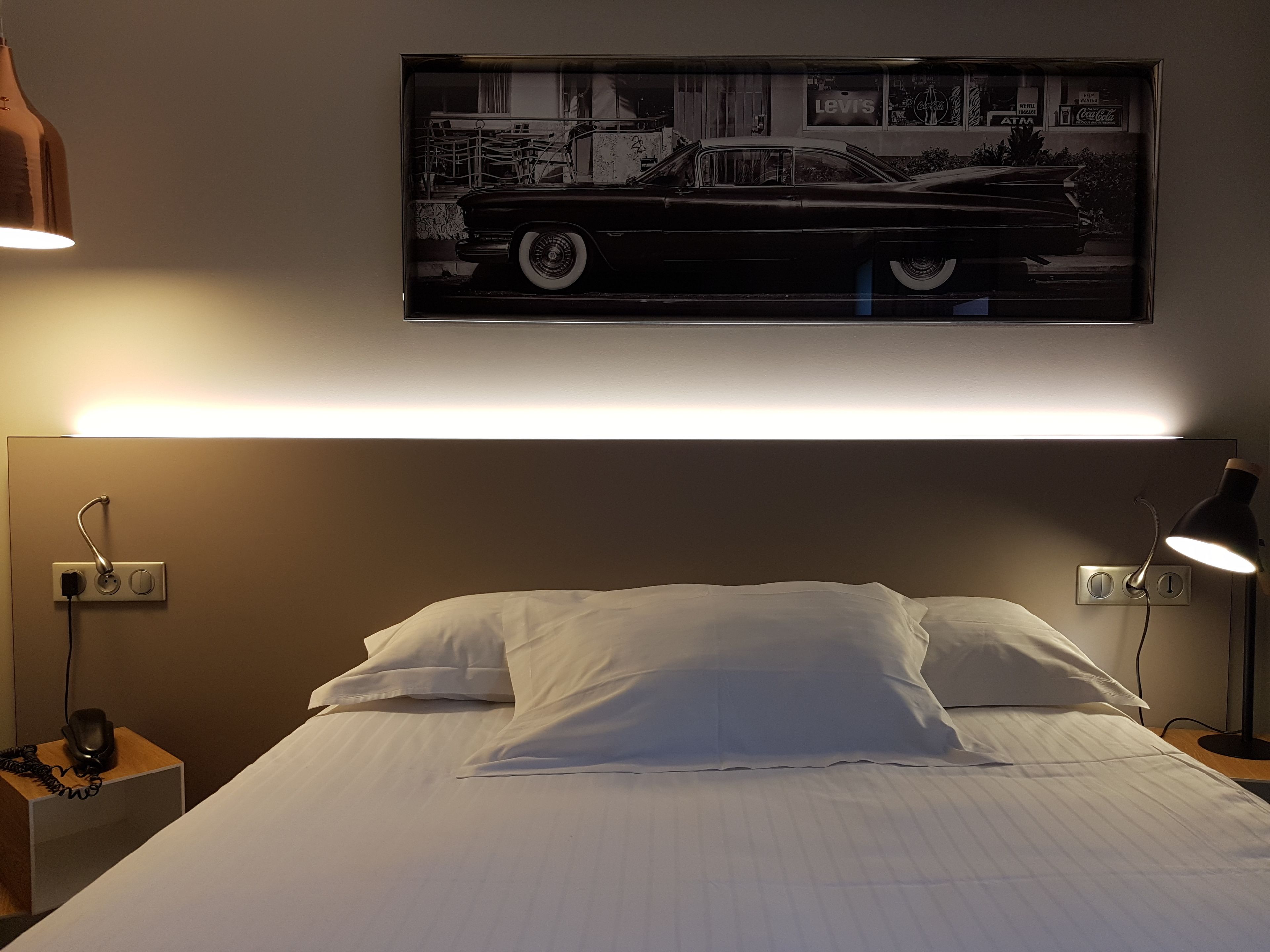 A hotel room with a bed, bedside lamps, a telephone, and a framed picture on the wall.