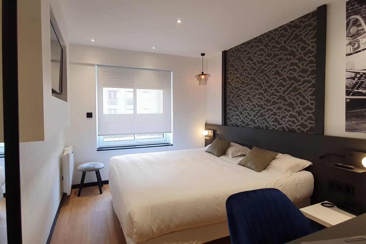 A modern bedroom with a large bed, a desk, and a wall-mounted TV.