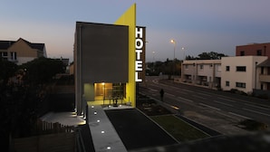 A modern hotel with a prominent 'HOTEL' sign, a well-lit entrance, and a street view with other buildings. - The Originals Boutique, Hotel La Chaussairie, Rennes (Chartres-de-Bretagne)