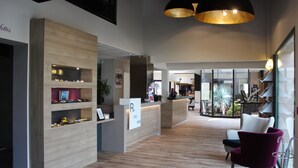 A modern reception area with wooden shelving, a reception desk, and a seating area with a purple chair. - The Originals Boutique, Hotel La Chaussairie, Rennes (Chartres-de-Bretagne)
