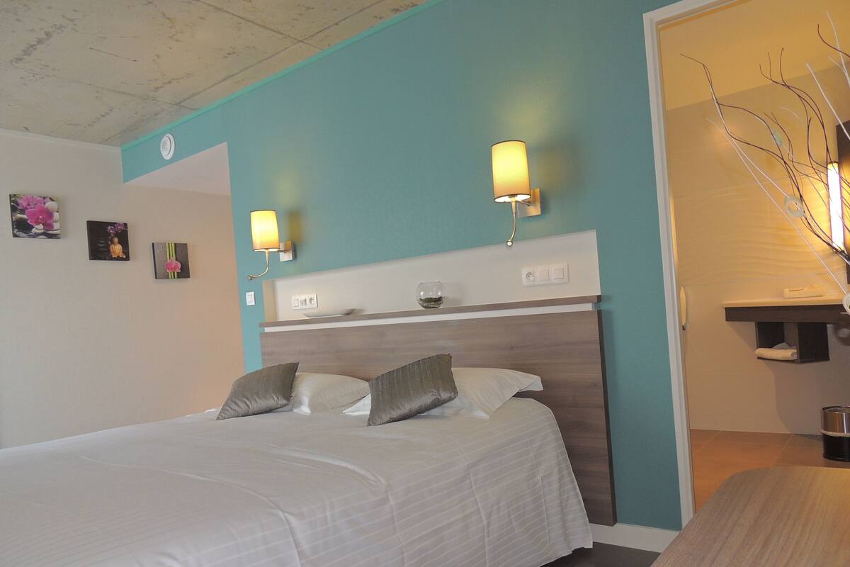 A neatly made bed with pillows, a bedside table, and a wall-mounted lamp.