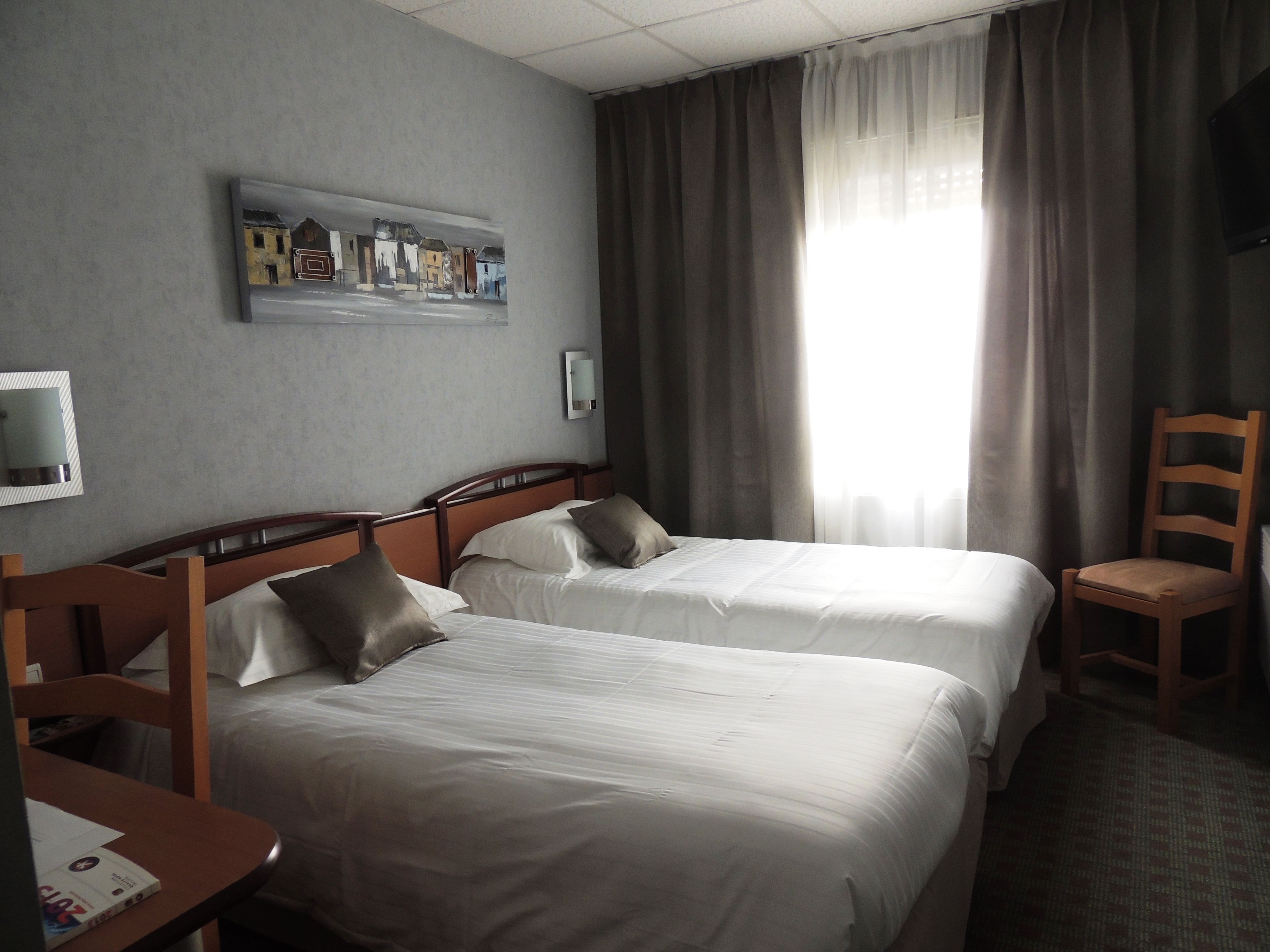 Ein Hotelzimmer mit zwei Betten, einem Holzstuhl, einem Fernseher und einem Gemälde an der Wand.