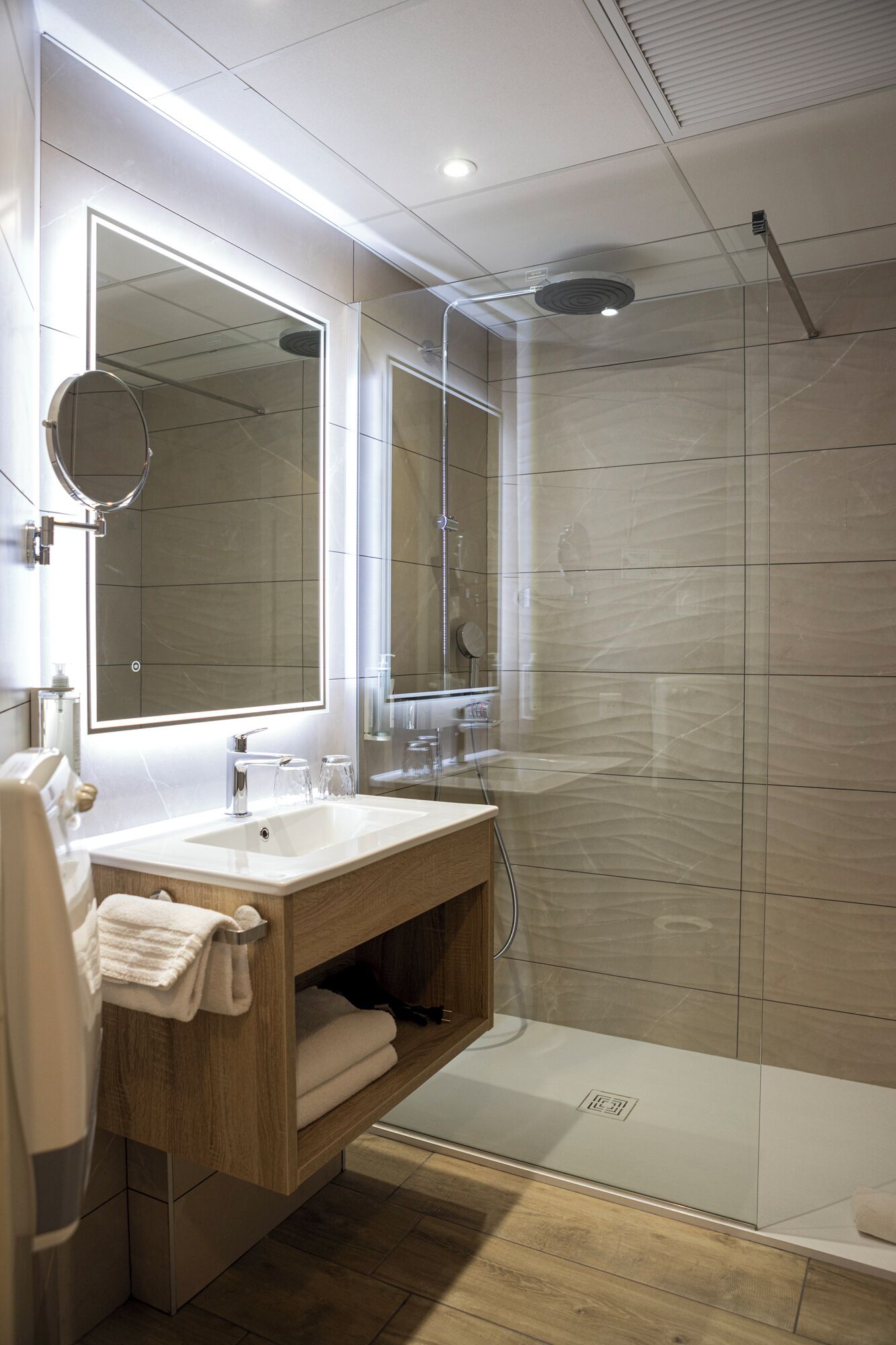 A modern bathroom with a glass shower enclosure, a large mirror, and a wooden vanity.