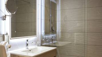 A modern bathroom with a glass shower enclosure, a large mirror, and a wooden vanity.