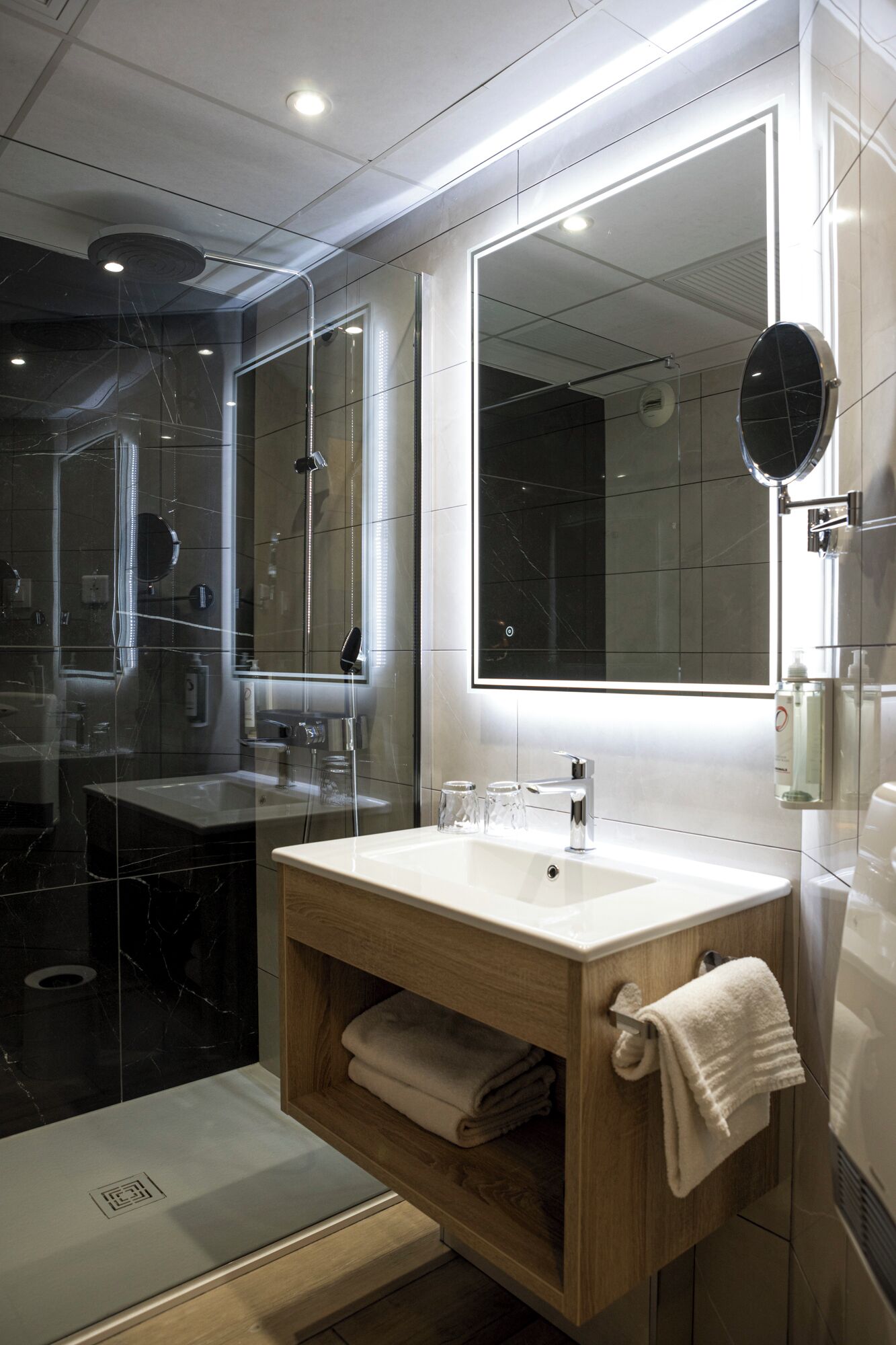 A modern bathroom with a large mirror, a sink, and a glass-enclosed shower.