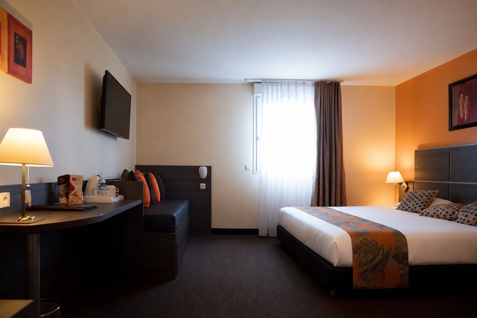 A hotel room with a bed, a desk, a chair, a television, and a window with curtains.